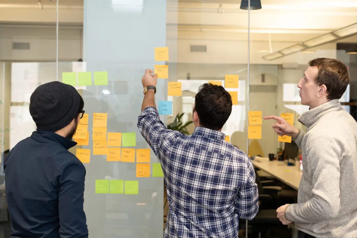 Three people work together on a sticky note exercise on a wall in one of the Enigma conference rooms.